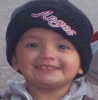 Yonatan Aguilar, a boy of about four or five years old, has fair skin and is smiling at the camera. He is wearing a black knit cap embroidered with the word "Angel".