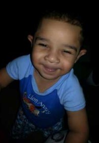 Photo of Princeton Holloway, a toddler boy with tan skin and dark curly hair, photographed from above and looking up at the camera.