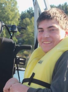 Photo of Theron Leonard. He is a young man with fair skin and short brown hair. He is wearing a gray sweatshirt and a yellow life vest and smiling at the camera.