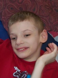 Photo of Austin Anderson, a thin boy with fair skin and dark blond hair. He is holding a hand near his face and smiling.