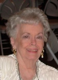 Photo of Shirley Neumann, an elderly woman with short gray hair and fair, wrinkled skin. She is wearing a white blouse and pearl earrings.