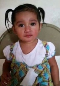 Photo of Leslie Ramirez. She is a small girl with tan skin and dark brown hair pulled into two ponytails. She is wearing a white shirt with a checked pinafore.