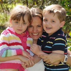 Photo of Maria, Elisa, and Martin Lutz, a mother and two children. Maria is hugging her two children, who are wearing brightly-colored clothing. They are all fair-skinned with light brown hair.