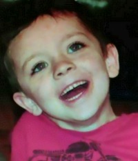 Photo of Tyler Caudill, a young boy with fair skin and brown hair. He has a wide smile. He is wearing a magenta T-shirt.