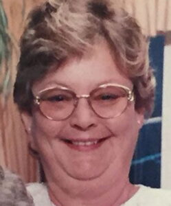 Photo of Patricia Swink, a heavyset middle-aged woman with glasses, smiling. She has short wavy blond hair and fair skin, and her make-up is neatly done.