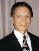 Photograph of Vincent Apilado, an older man in a suit and tie. He has dark brown, graying hair and olive-toned skin.