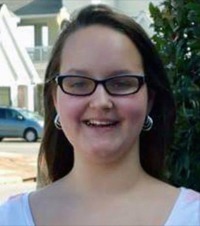 Photo of Grace Packer. She is a teenage girl with fair skin and straight brown hair. She is wearing hoop earrings, black-rimmed glasses, and a white flowered shirt.