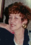 Photo of Barbara Martone. She is a woman with auburn hair and fair skin, wearig pink lipstick and nail polish, gold earrings, and a black and gray blouse.