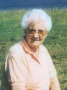 Photo of Addison Avis, an elder woman with short, curly white hair and fair skin. She is wearing a pale peach blouse and tinted glasses, and is smiling for the camera.
