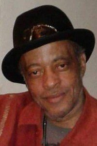 Photo of Walter Clark. He has brown skin; he is wearing a black hat and a red collared shirt.