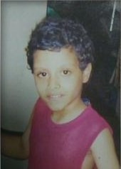Photo of Matthew Tirado, a young boy with light-brown skin and curly black hair. He is wearing a red tank top.
