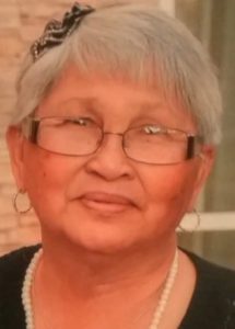 Photo of Gertrudes Hollis, an older woman with tan skin and a black-and-white ribbon in her short white hair, wearing glasses and a pearl necklace.