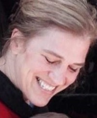 Photo of Roberta Rybinski, a woman with fair skin and blonde hair. She is grinning with her eyes squeezed shut, as though she is laughing at a joke.