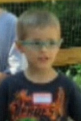 Photo of Daniel Schlemmer, a young boy wearing glasses and a navy T-shirt with a name tag on it. He has short blond hair and fair skin.