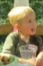 Photo of Luke Schlemmer, a toddler boy with fair skin and blond hair. He is sticking his tongue out and smiling.
