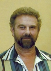 Portrait of David Leath. He is a middle-aged man with curly brown hair and beard and light skin; he is wearing a striped shirt.