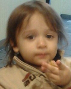 Slightly blurred photo of Michael Guzman, a Caucasian toddler with wispy brown hair, wearing a brown sweater and holding his hand out to the camera.