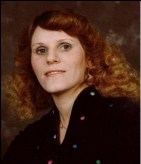 Portrait photo of Shirley Williamson, a middle-aged woman with pale skin and curly, shoulder-length auburn hair.