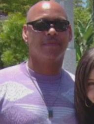 Photo of Reuben Johnson, a man with light-tan skin. He is wearing sunglasses and a pink and white sweatshirt; his face and head are both clean-shaven. Off to the side of the photo is a young girl with brown hair and light-tan skin.