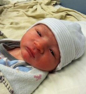 Photo of Gabriel McFarland, a newborn baby with pink skin, wearing a cotton hat and pale blue sweater.