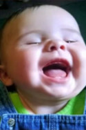 Photo of L'Naya White, a baby with her mouth open and eyes squeezed shut in laughter. She has fair skin. She is wearing a green and blue top.