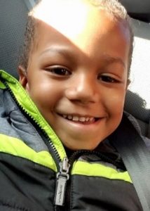 Photo of Antonio di Stasio, a young boy with brown skin and very short brown hair. He is smiling at the camera, and wearing a black jacket with bright yellow stripes.