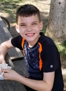 Photo of Dylan Davis, a boy with short brown hair and fair skin, photographed outdoors. He is grinning at the camera.