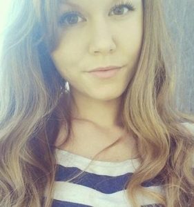 Photo of Jaylynn Keith, a young woman with light skin, brown eyes, and wavy blonde hair. Her light makeup is carefully applied and she is wearing a blue-and-white top. The photo is somewhat overexposed and taken from close-up, probably a selfie.
