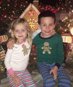 Photo of Luke and Bree Dawson, two small children. Bree is a girl with blond hair and fair skin; Luke has dark hair and fair skin. They are wearing Christmas-themed gingerbread cookie sweaters and have their arms around each other.