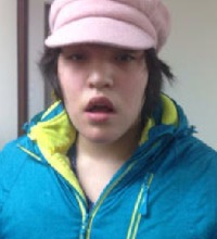 Photo of Lydia Whitford, a young woman with pale skin and short brown hair, wearing a neon yellow and turquoise jacket and pink ball cap. 