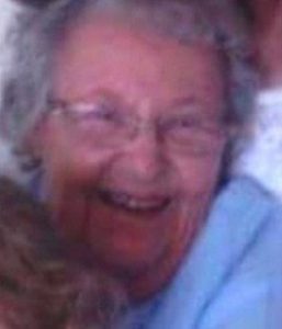 Photo of Betty Guy, an elderly woman with light skin and light-gray hair, wearing glasses and a blue top. She is smiling and hugging someone off-camera.