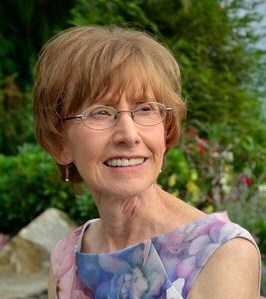 Photo of Essie Swanson, a middle-aged woman with short light-brown hair, fair skin, and glasses, wearing a sundress and photographed outside.