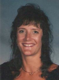 Photo of Deborah Crouch, a middle-aged woman with light skin and curly dark-brown hair. She is wearing a gold pendant necklace and smiling, showing a gap between her front teeth.