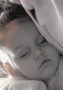 Photo of a sleeping fair-skinned toddler girl, draped in cloth.