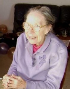 Photo of Marcia Clark. She is a thin elderly woman with pale skin and gray hair, wearing glasses and a purple long-sleeved shirt. 