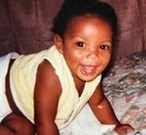 Photo of Katonya Jackson, a baby with dark-brown skin and curly black hair. She is crawling on hands and knees and smiling broadly at the camera. She is wearing a white shirt and diaper.