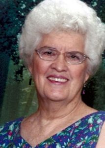 Photo of Jeanette Brown, an elderly woman with permed white hair and fair skin, wearing glasses and a blue patterned dress.