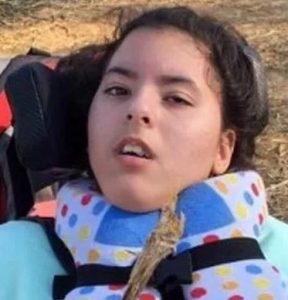  Photo of Aurelia Castillo, a teenage girl with dark curly hair and olive-toned skin. She is sitting in a wheelchair, and wearing a polka-dotted neck brace. 