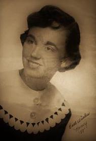 Old, sepia-tone portrait photo of Nancy Gleisinger. She is a young woman with fair skin and curly dark-brown hair, wearing a shirt with a broad white collar. Writing at the bottom of the photo says, "Best wishes, Nancy. '58."