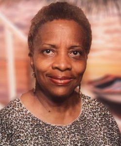 Photo of Bertha McGill, a middle-aged African-American woman with her hair cut quite short. She is wearing a leopard-print shirt and dangle earrings.