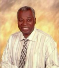 Portrait photo of Philip White. He is a middle-aged man with graying curly black hair and dark-brown skin, wearing a dress shirt and tie.