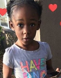 Photo of Je'Hyrah Daniels, an African-American toddler with tightly braided hair, wearing a T-shirt printed with "Have Fun". She is looking at the camera with her mouth pursed in fascination, and holding a cell phone.