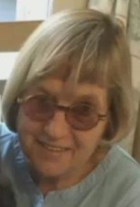 Photo of Ann DeLucia, an elderly woman with pale skin and chin-length white hair, wearing a pair of round sunglasses.