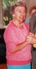 Photo of Louise Papeman, an elderly woman in a pink sweater, with short gray hair, smiling at the camera and holding on to someone's hands off-frame.
