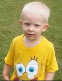 Photo of a toddler boy with very fair hair and pale skin. He is looking at the camera with a slightly puzzled expression. He is wearing a yellow SpongeBob T-shirt.