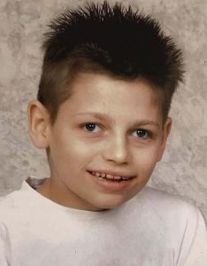 School photo of a boy with brown spiky hair, wearing a white T-shirt.