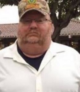 Photo of John Likeness, a heavyset man with muttonchops, wearing glasses and a camo baseball cap.