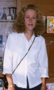 Photo of a young woman with curly blonde hair and fair skin, wearing a white blouse.