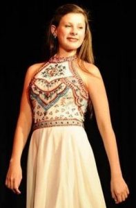 Photo of Emily Hampshire, a teen girl in a traditional dancing dress with an embroidered top and long, white flowing skirt. She has long straight dark-blond hair and is posing for dance.