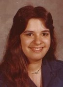 Portrait photo of Kelly Barber, a woman with thick brown hair and fair skin, wearing a thin silver necklace and suit jacket; she is smiling.